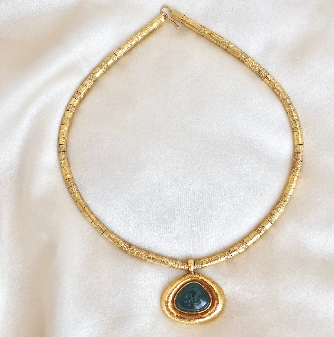 An 18K gold chain necklace with a textured, segmented design and a teardrop-shaped pendant featuring an intaglio carved Indicolite Tourmaline set in a domed bezel border.