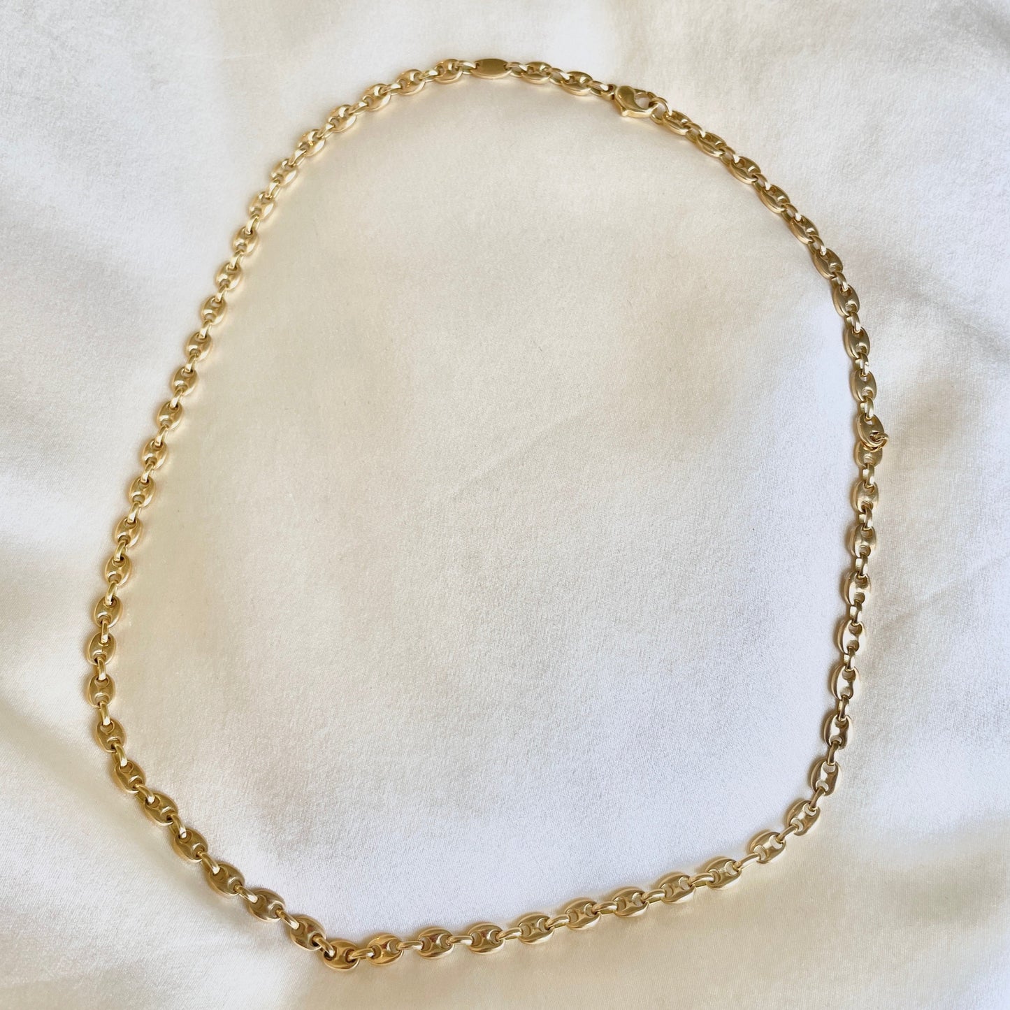 18k Gold puffy mariner chain necklace on a white fabric background solid link construction
