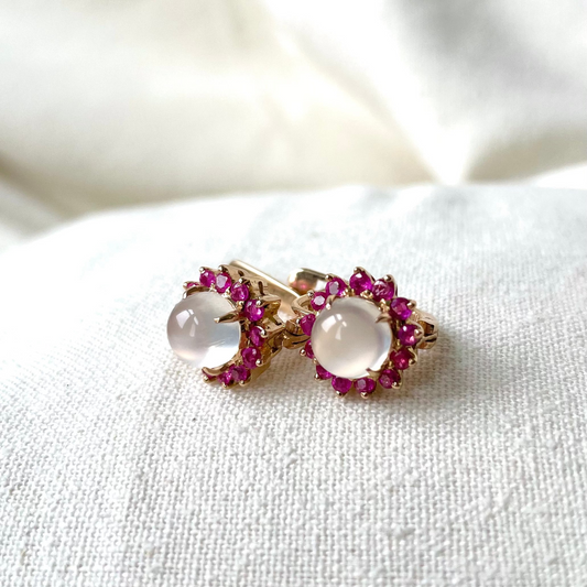 A pair of 14 K yellow gold lever back earrings with moonstone centers and ruby accents, placed on a white fabric surface.